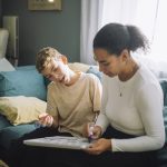 Mother and son preparing weekly planner while sitting on sofa at home